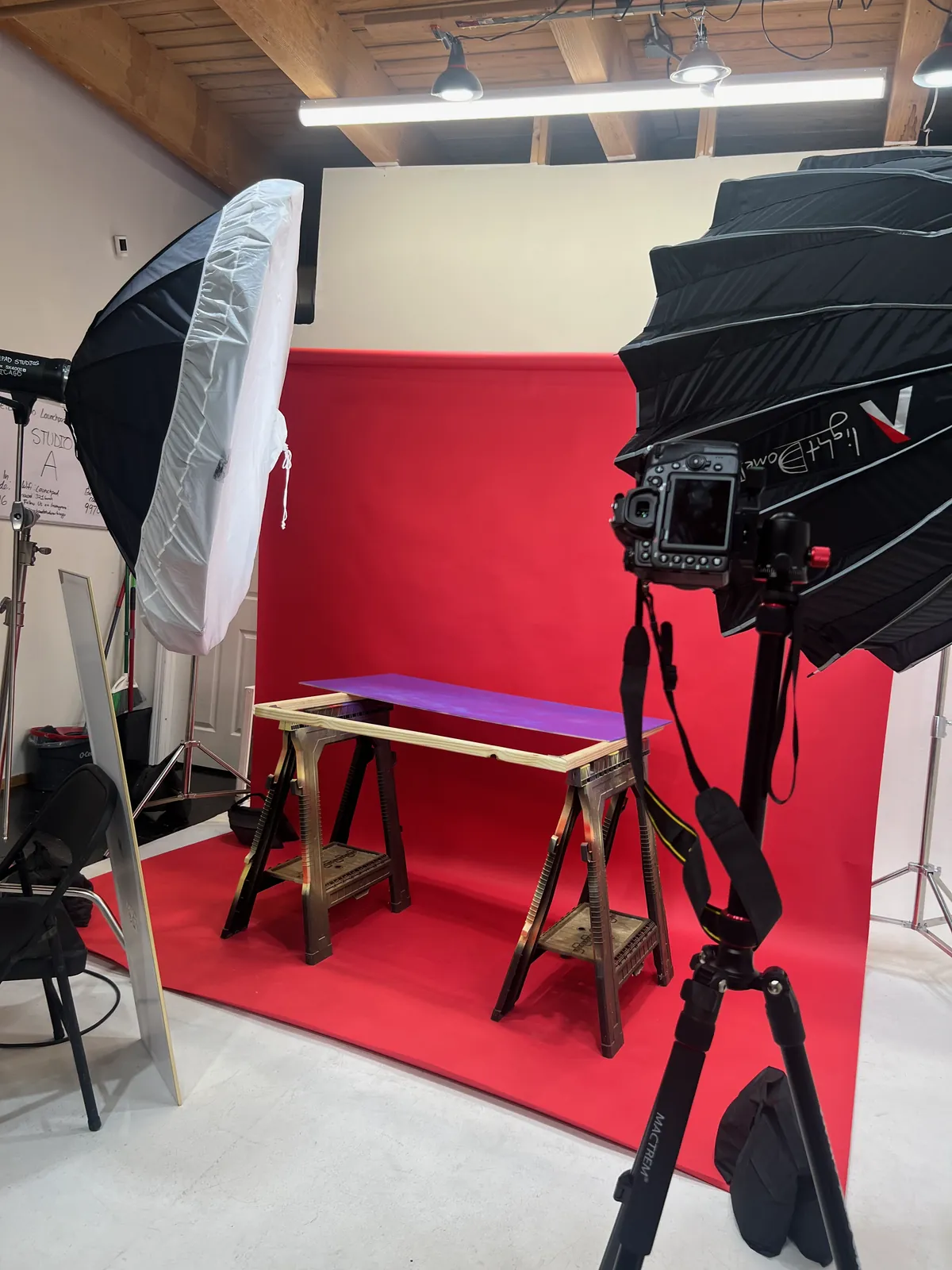 The studio before the shoot: softbox lights and a camera on a tripod, with the violet tabletop on sawhorses in front of the red backdrop.