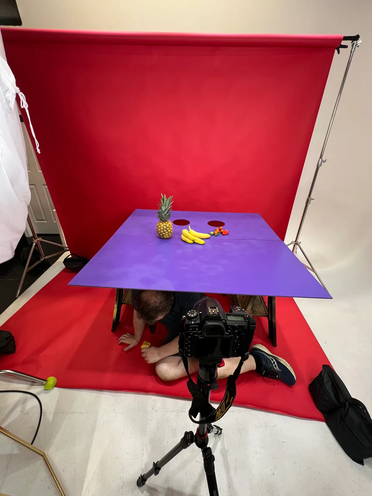 The full set: the red backdrop and violet table, with someone sitting underneath ready to reach up through the holes.