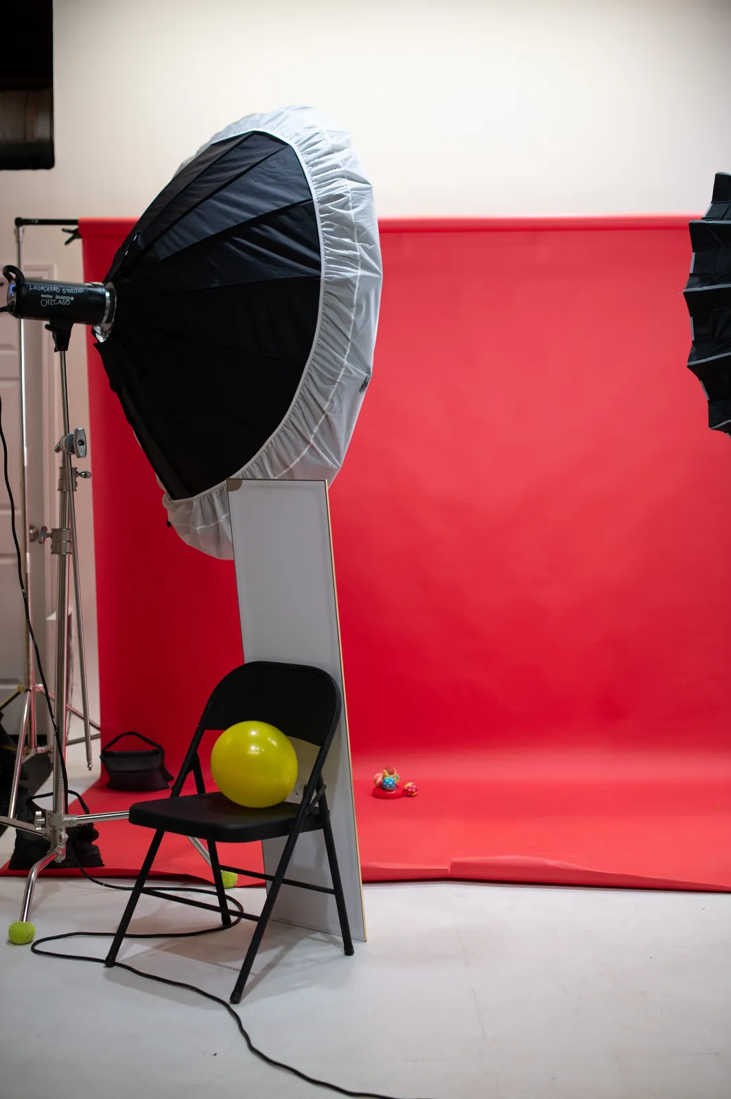 Monica's studio: a large softbox beside the red backdrop, with a yellow balloon waiting on a folding chair.