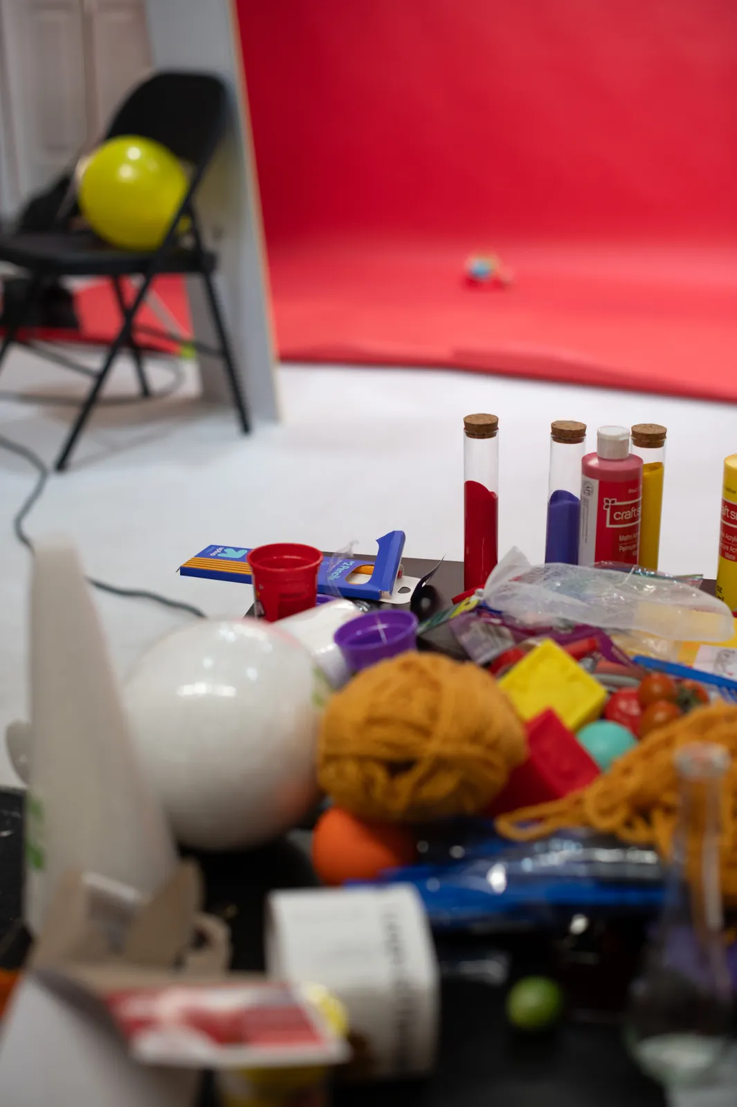 The props table: paint jars, yarn, balls and a yellow balloon, with the red set behind.