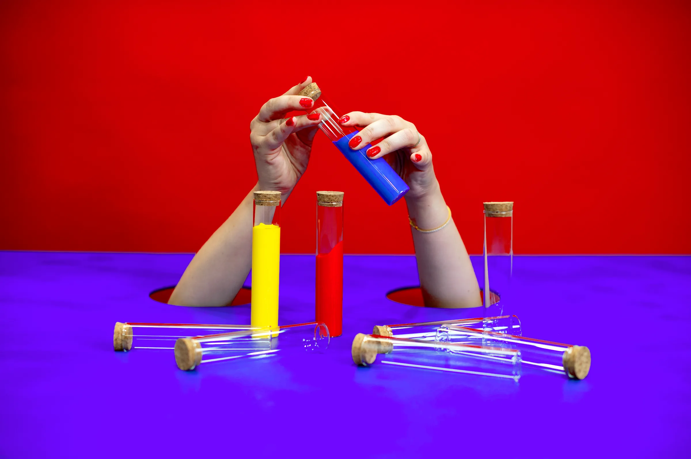 Hands pour coloured liquid between glass test tubes standing on the violet table.