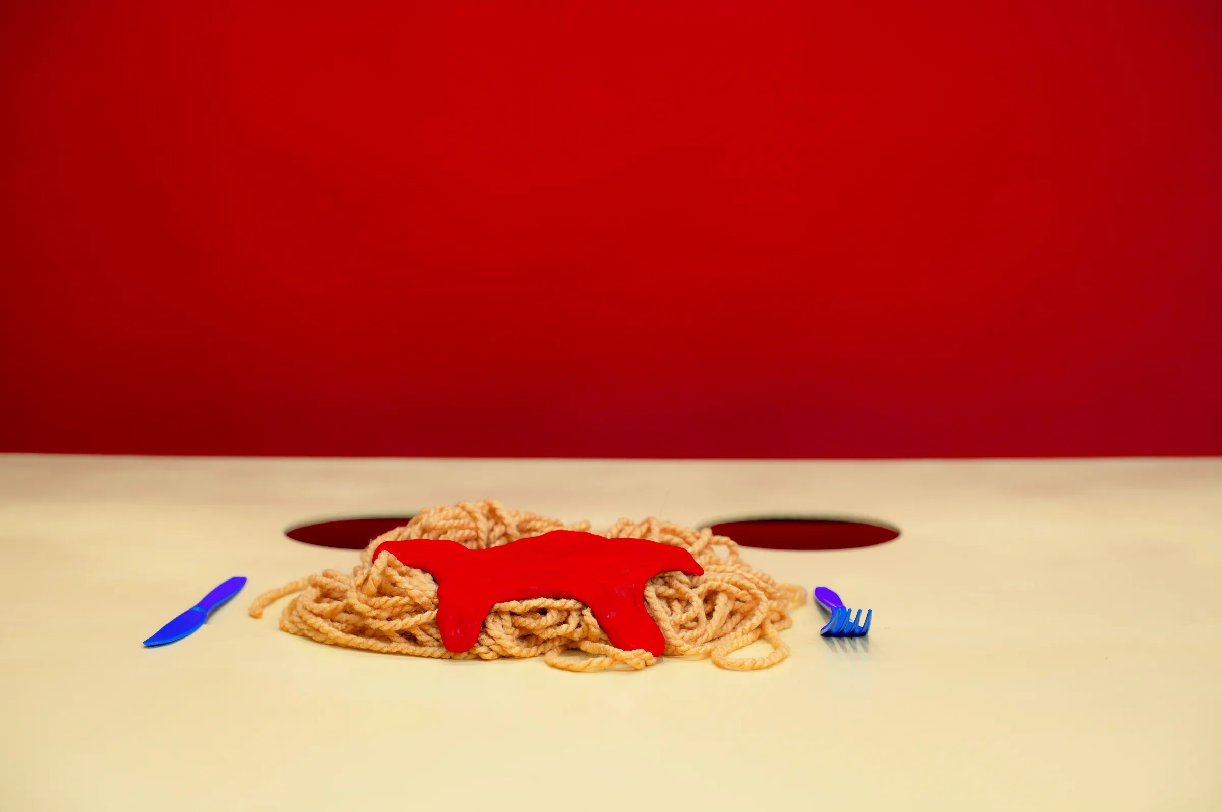 A plate of spaghetti with a red splat on a yellow table, a blue fork beside it.