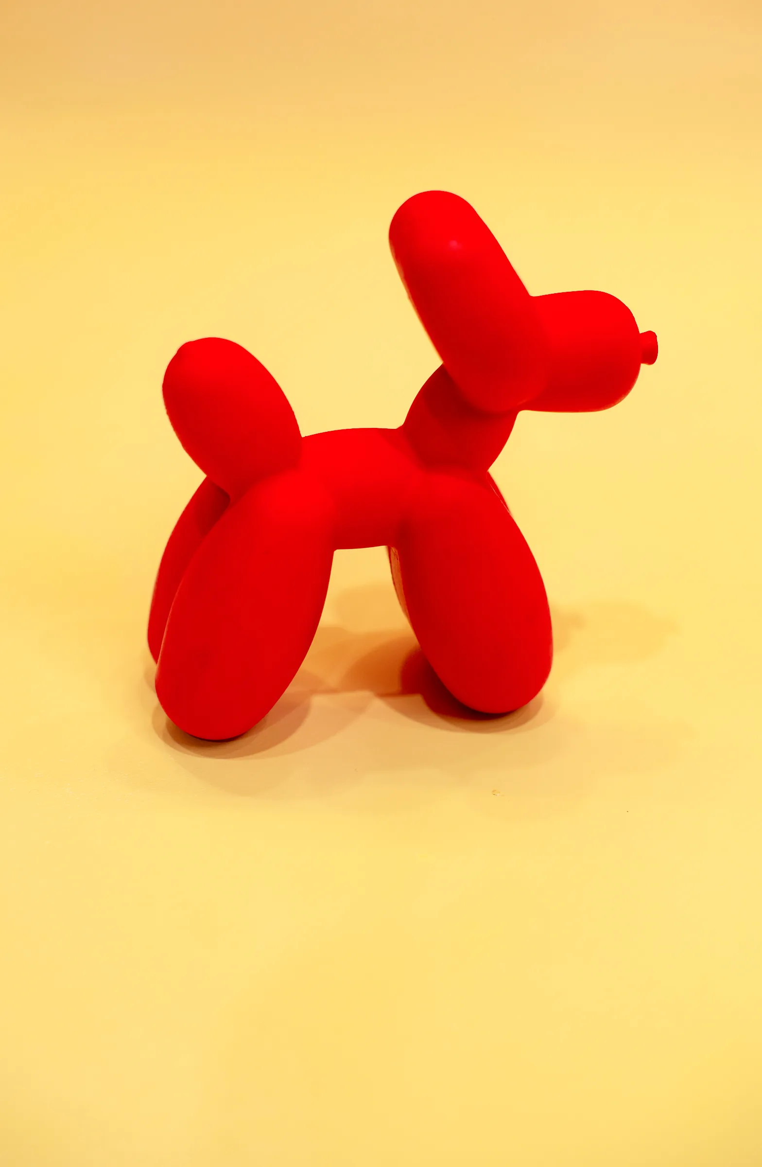 A red balloon dog on a yellow backdrop.