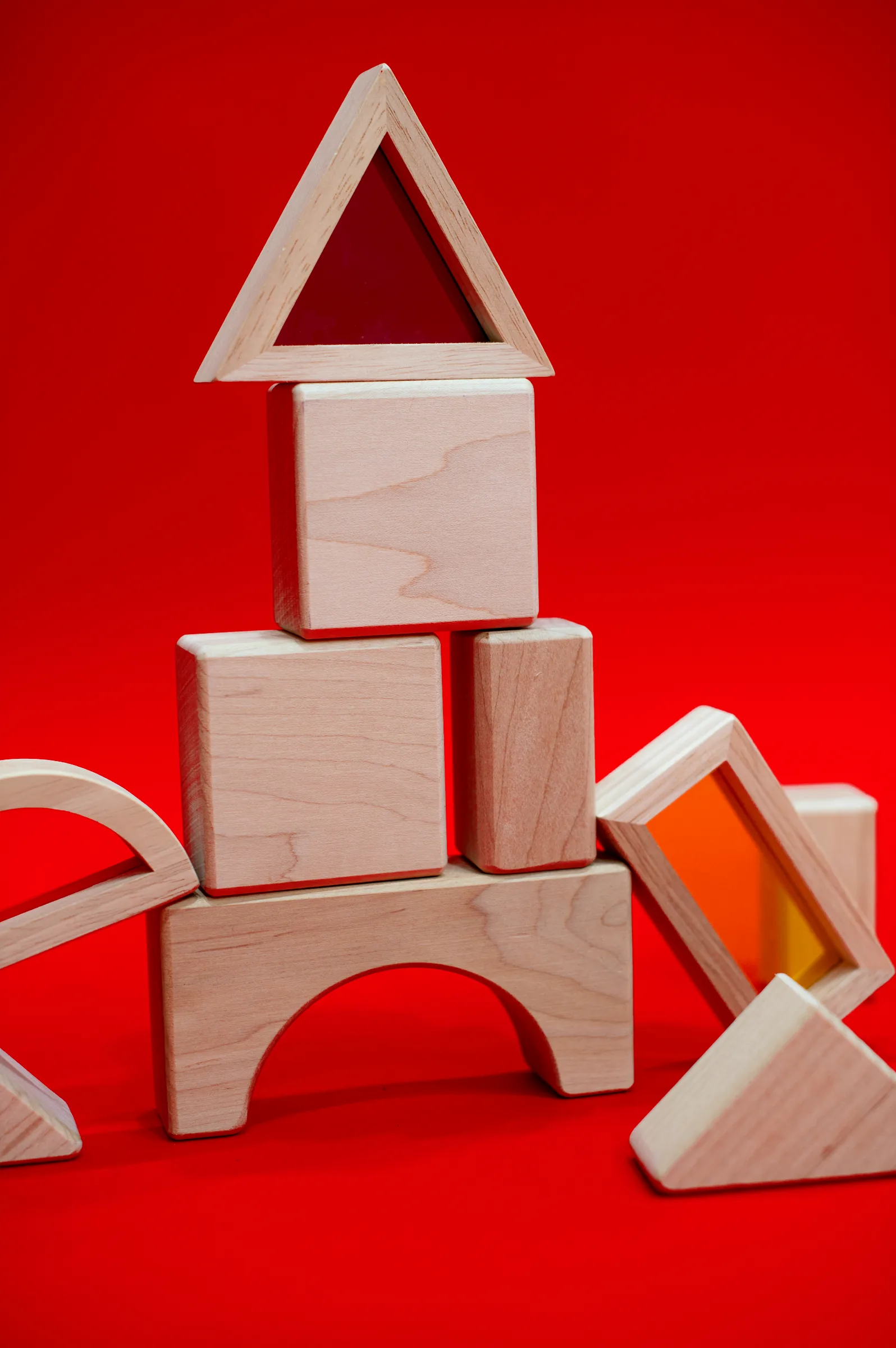 A tall tower of wooden blocks topped with a triangle, on red.